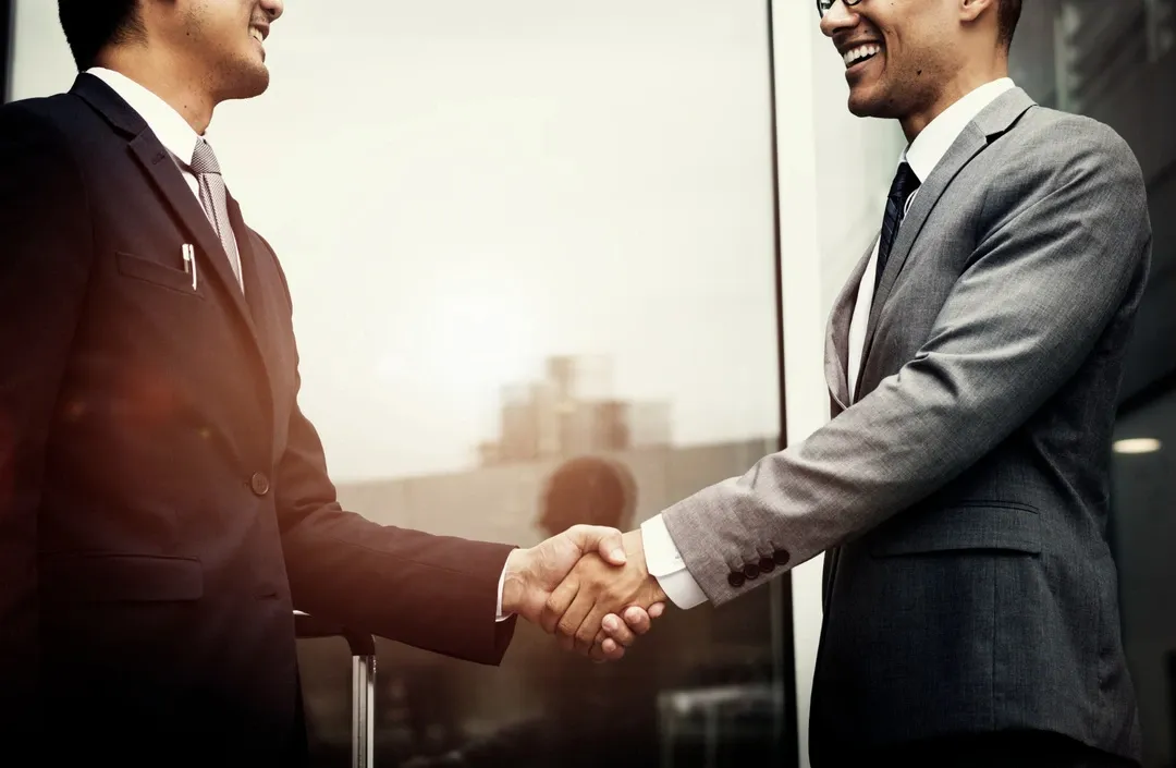 Two professionals shaking hands in an office, symbolizing strategic business partnerships