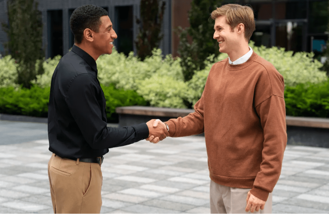 Two men shaking hands outdoors, smiling and making a business agreement