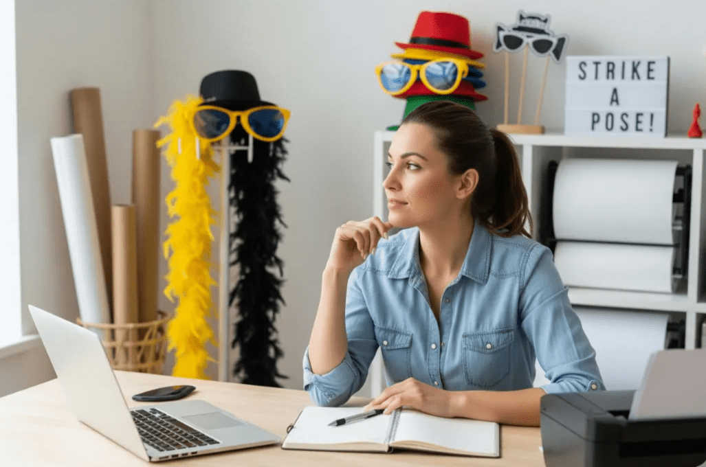 Photo booth business owner considering options with laptop and props nearby